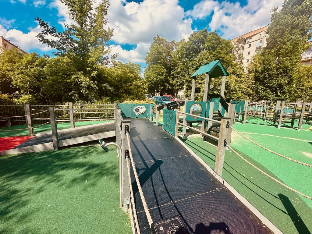 ire de jeux en plein air avec structures en matériaux recyclés, intégrée dans un environnement urbain et verdoyant