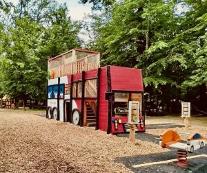Structure de jeu en bois en forme de bus scolaire avec des jeux ludiques, réalisée par un design studio et placée sur une aire de jeu.