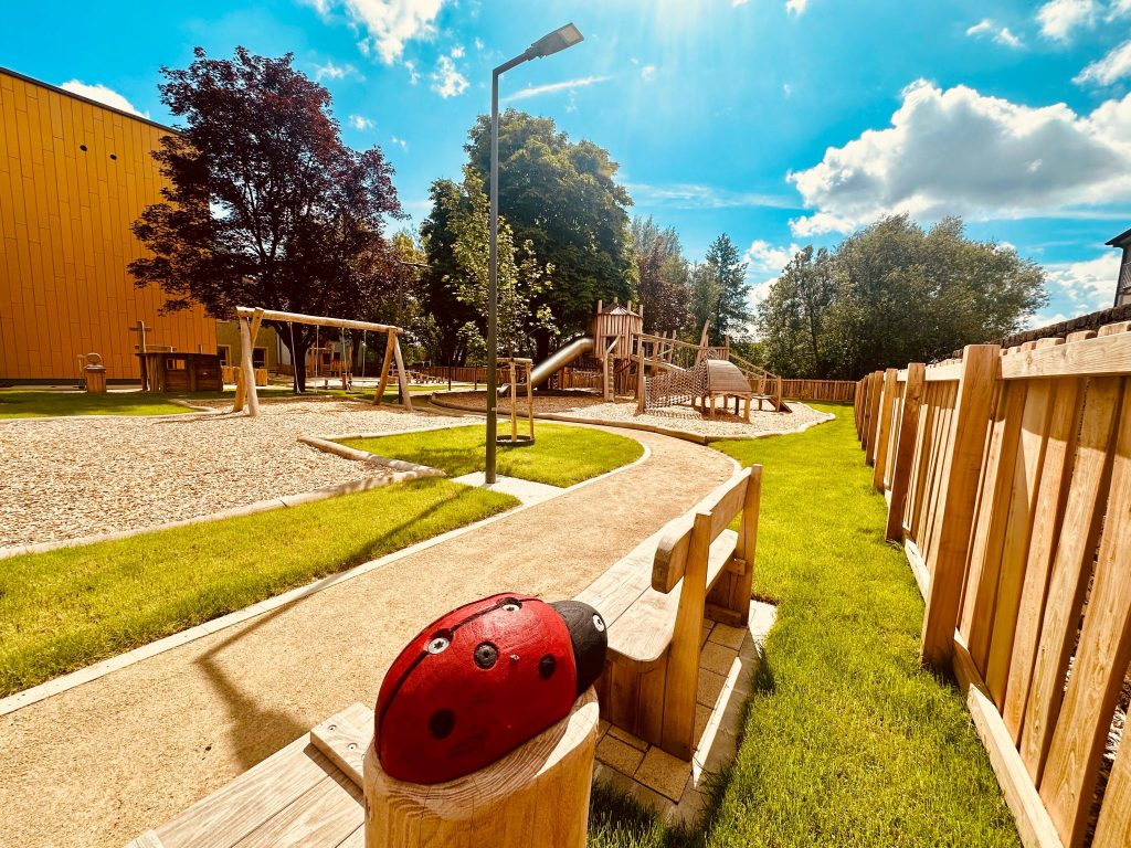 Aire de jeux extérieure en robinier sur mesure avec balançoires et structures en bois, dans un environnement sécurisé et verdoyant.